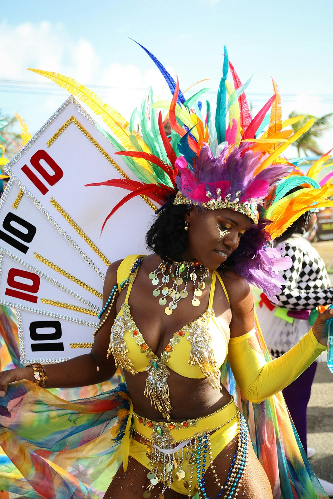 A woman wearing a yellow bikini and a multicolored headdress with playing cards attached as "wings" dances at Anguilla Carnival